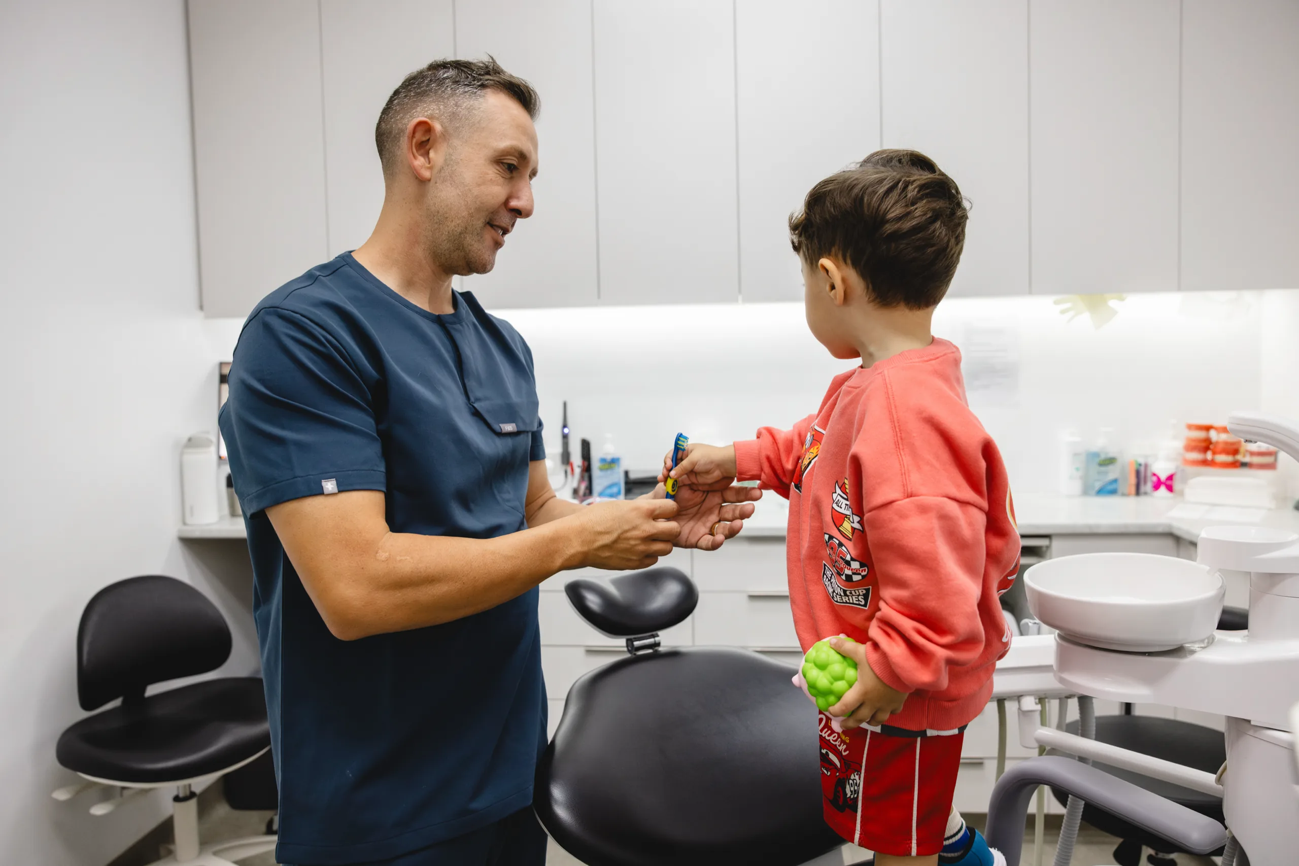 Anthony Adaimy handing a toothbrush to a young boy in the surgery