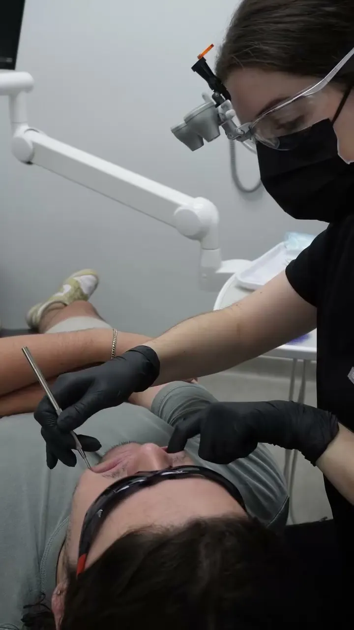 Dr Rachel Brown in loupes and gloves checking a patient’s teeth with instruments