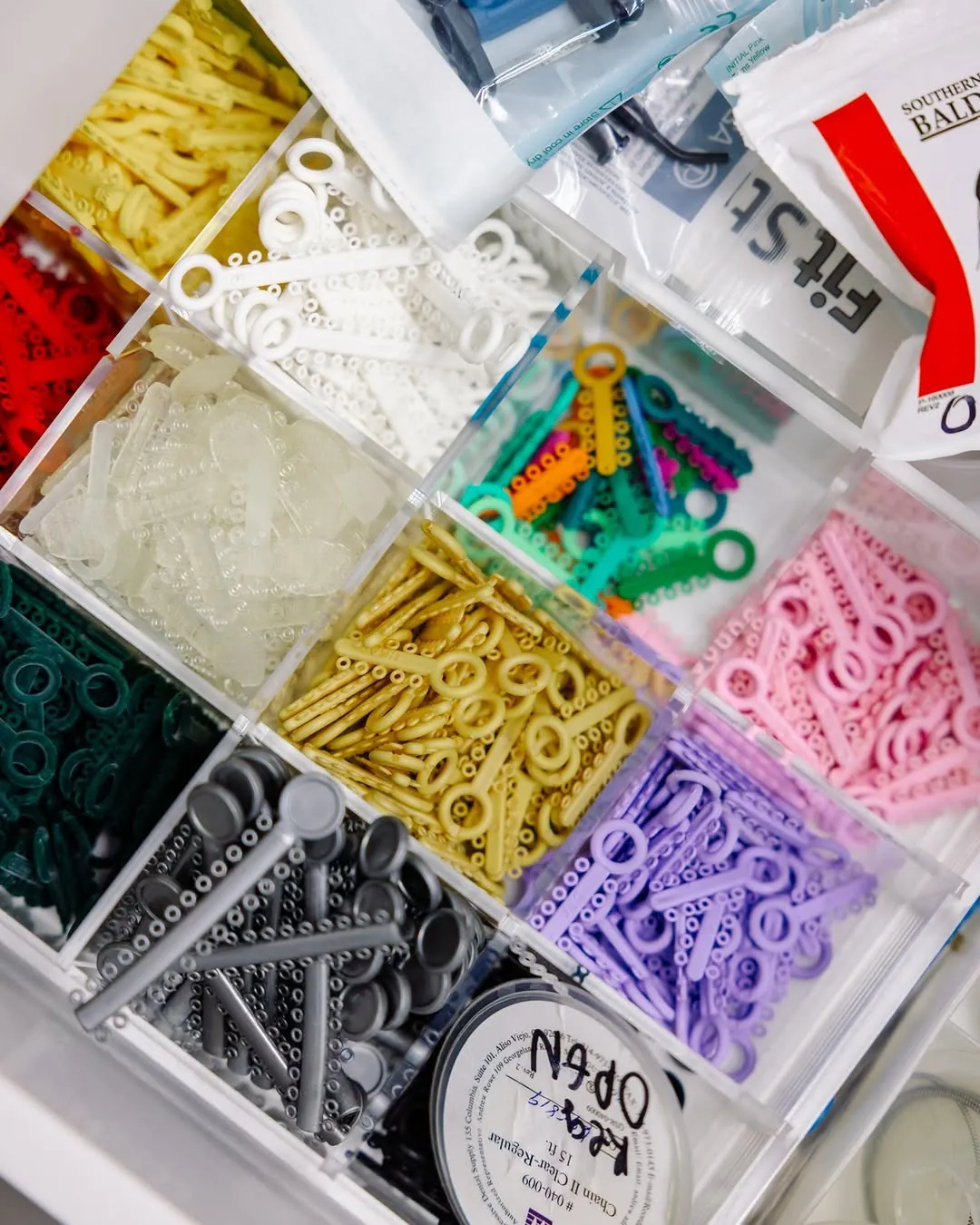 A drawer of coloured elastic bands for braces, sorted by colour
