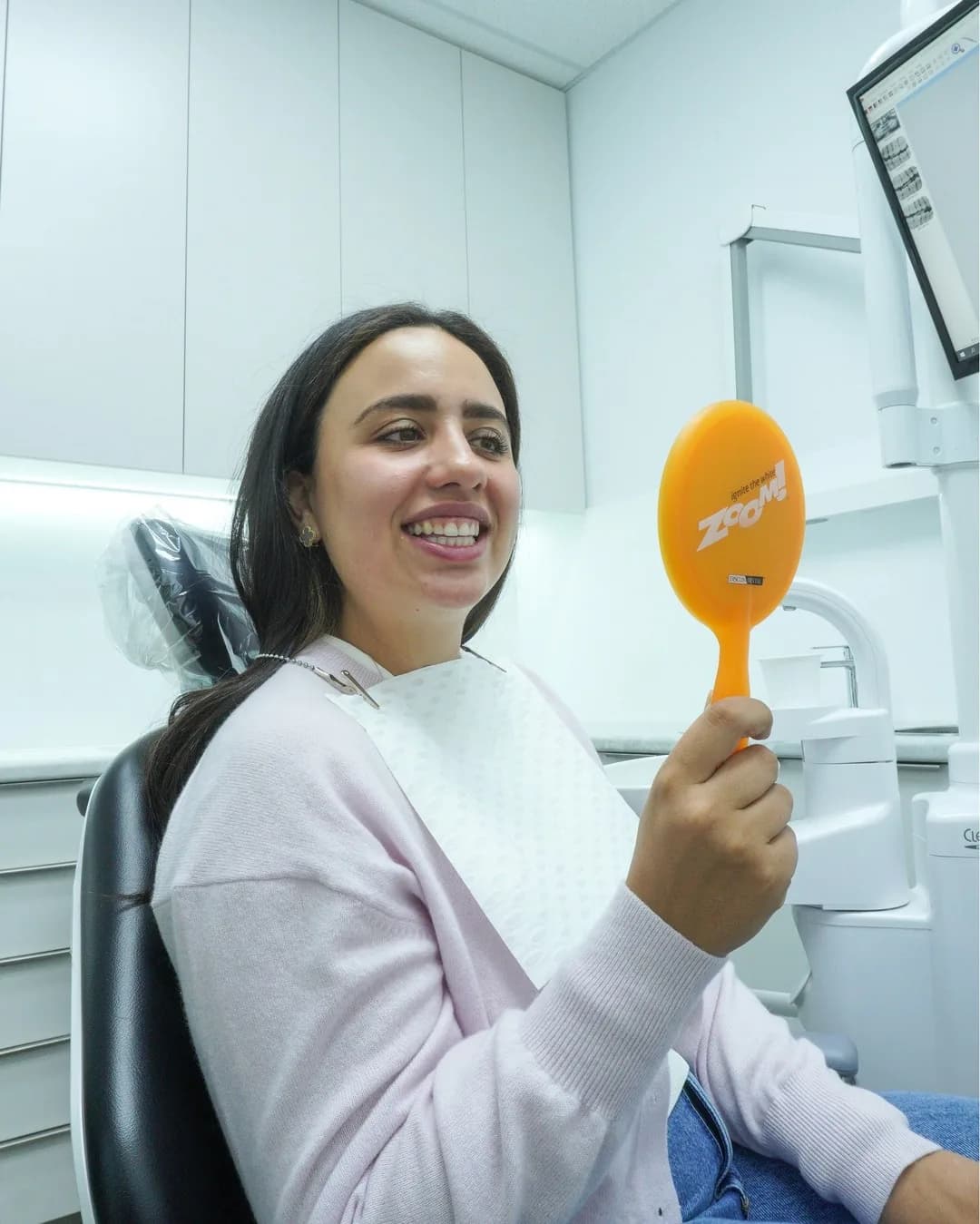 A patient checking her smile in a hand mirror at Dental Spot
