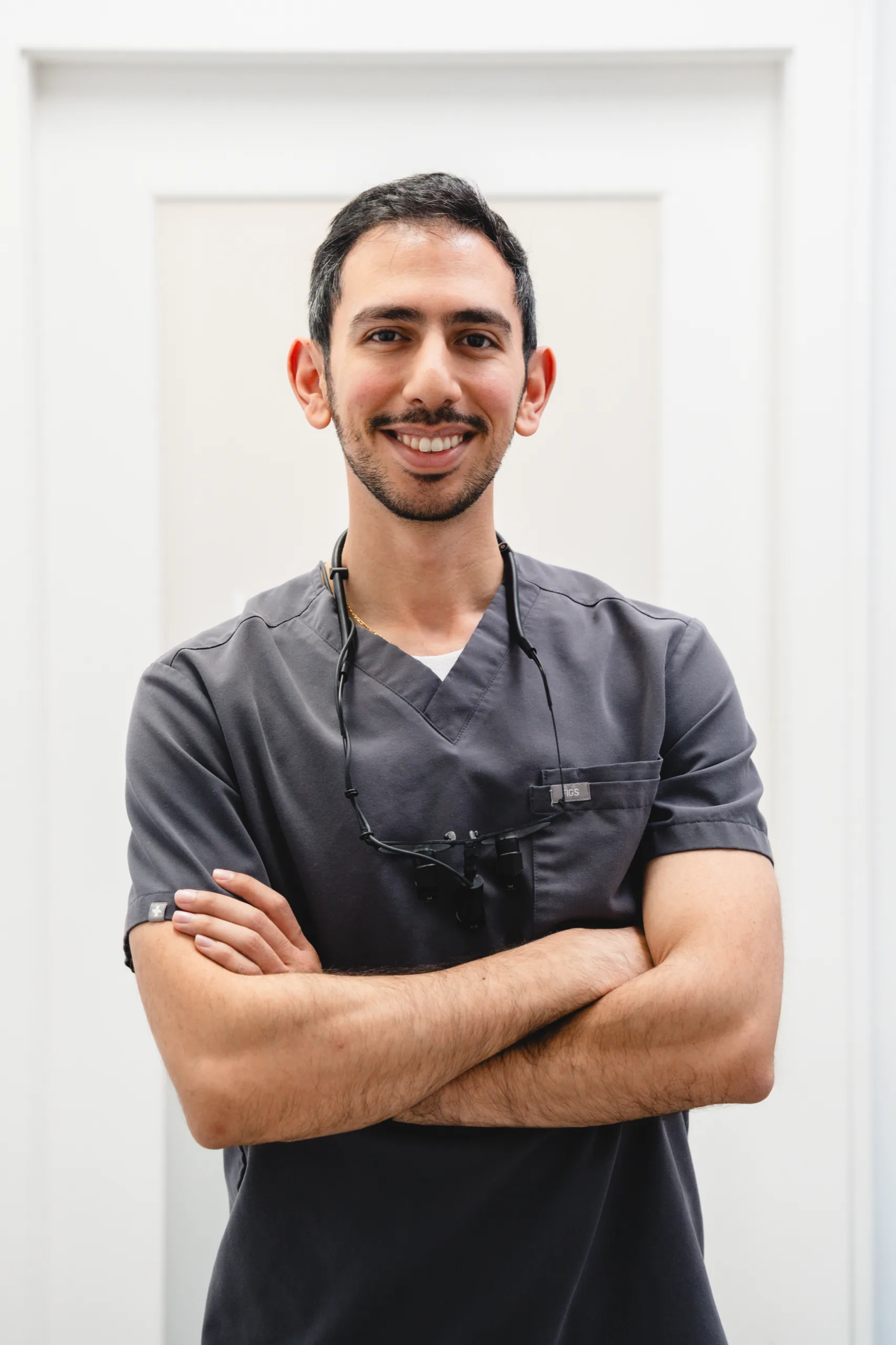Dr Jose Shina in grey scrubs, arms crossed, smiling