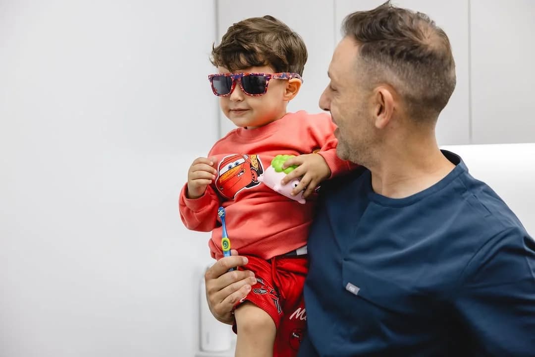 One of our dentists holding a young patient in sunglasses with a toothbrush