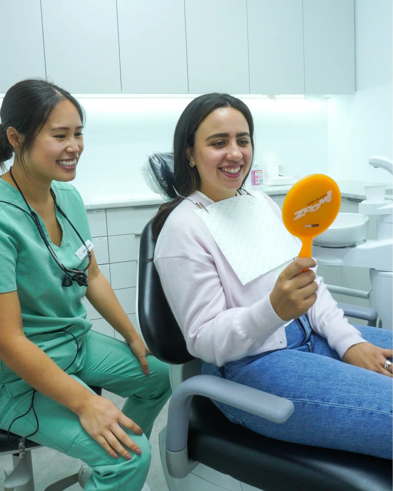 Dr Amanda Zhong talking with a patient, who checks her smile in a hand mirror