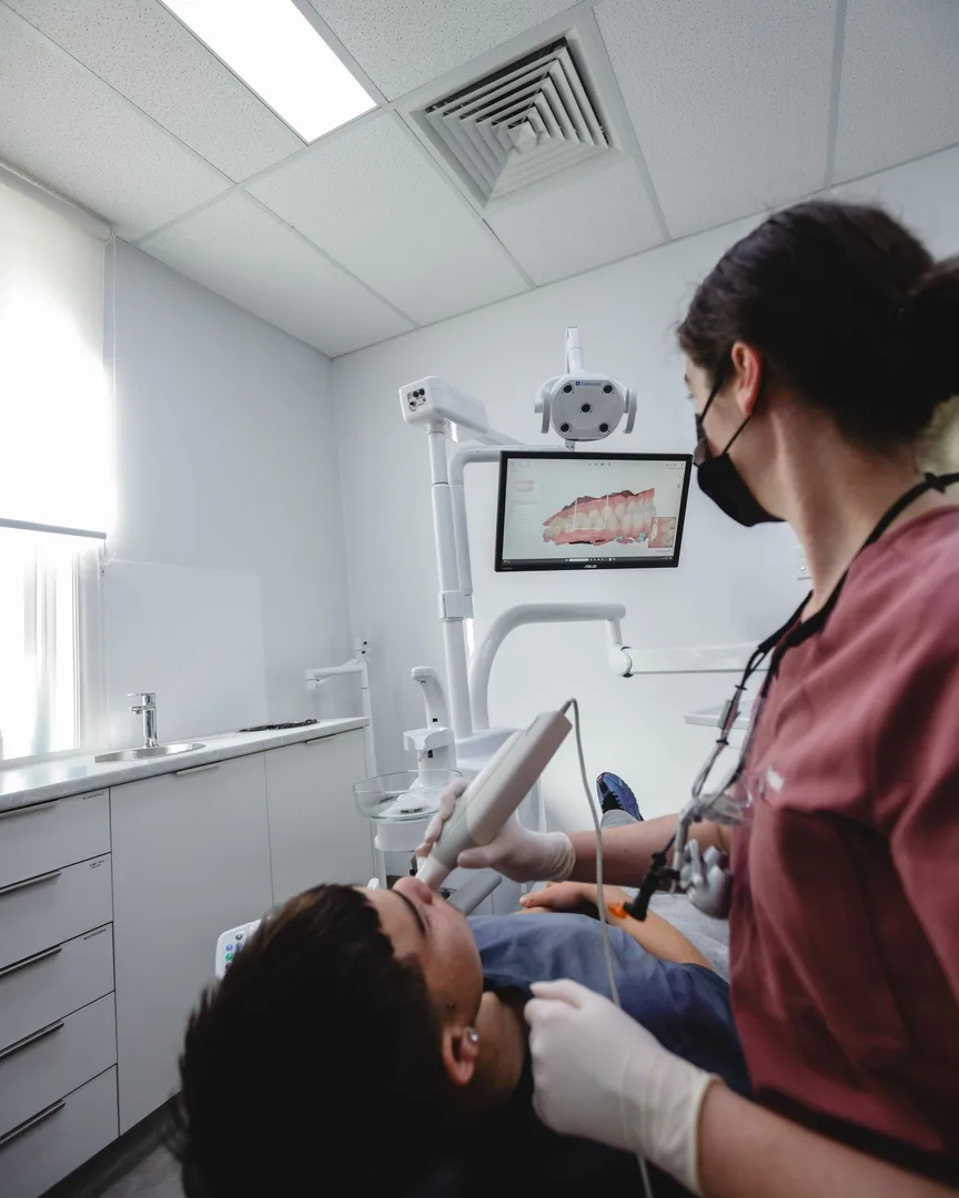 A dentist in mauve scrubs with a patient in the chair, a scan on the screen above.