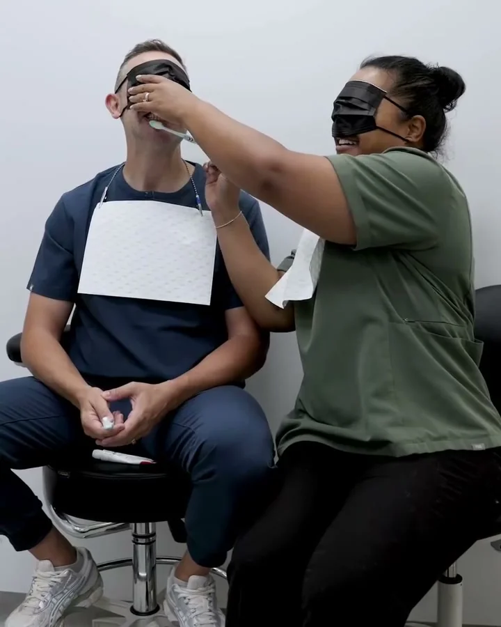 Two team members attempt a blindfolded toothbrushing challenge.
