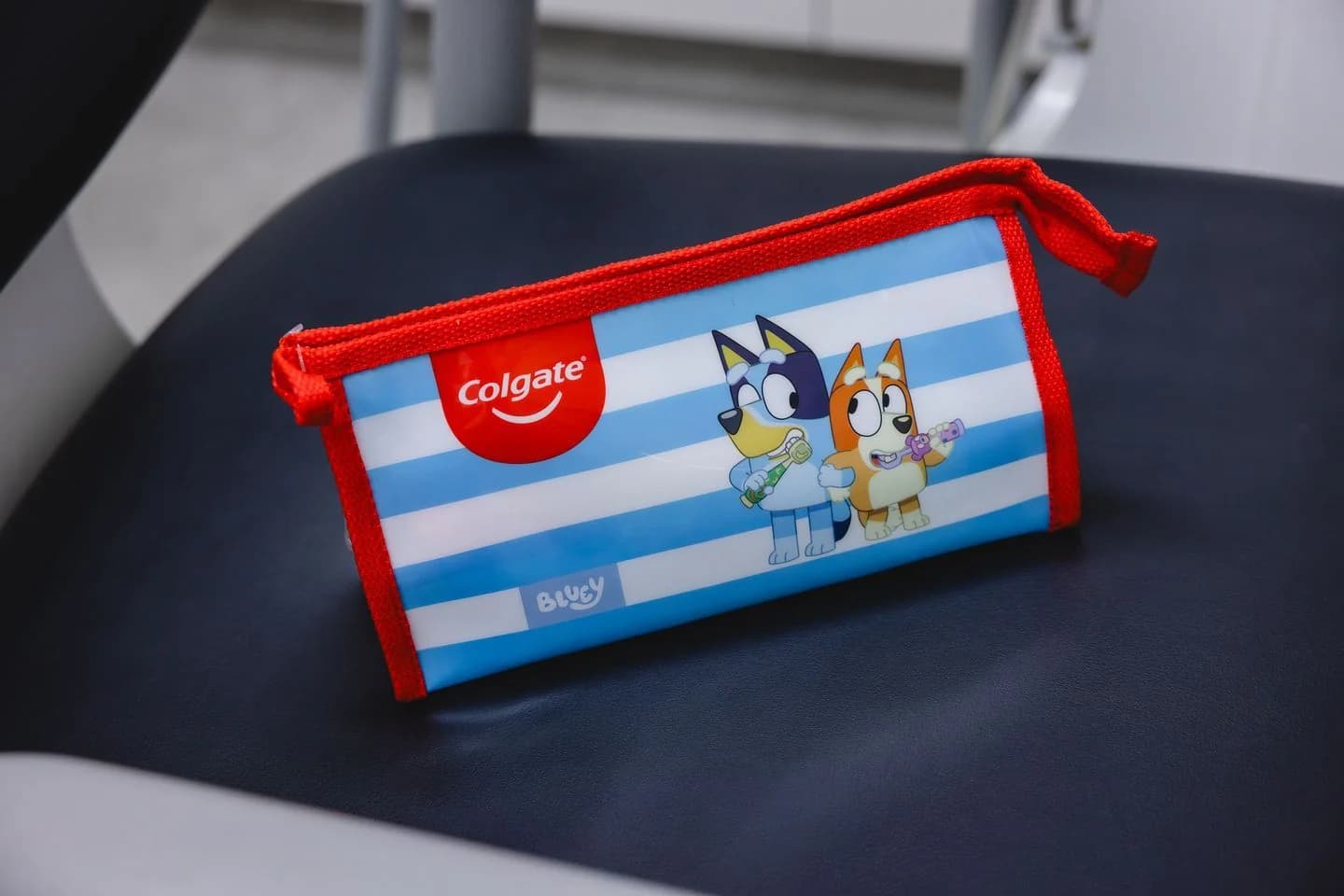 A blue and white striped Bluey dental kit pouch rests on a dark clinic chair.